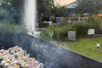 Miniature Traiteur Leers (Nord) - Tendance et Fraicheur Traiteur #20 Brochettes de viande et légumes grillant sur un barbecue en plein air, avec une fontaine et un jardin en arrière-plan.