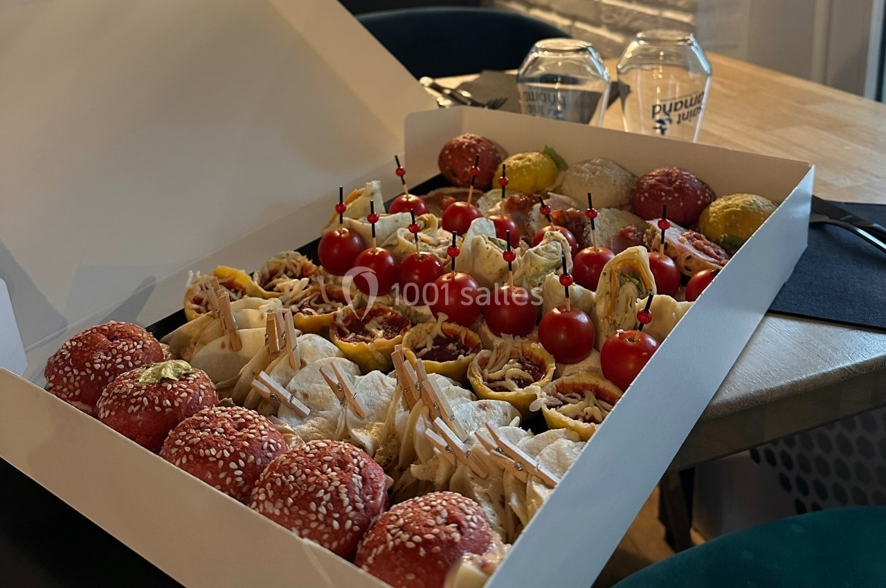 Plateau de mini-sandwiches variés, wraps et brochettes apéritives avec tomates cerises, présenté dans une boîte ouverte.