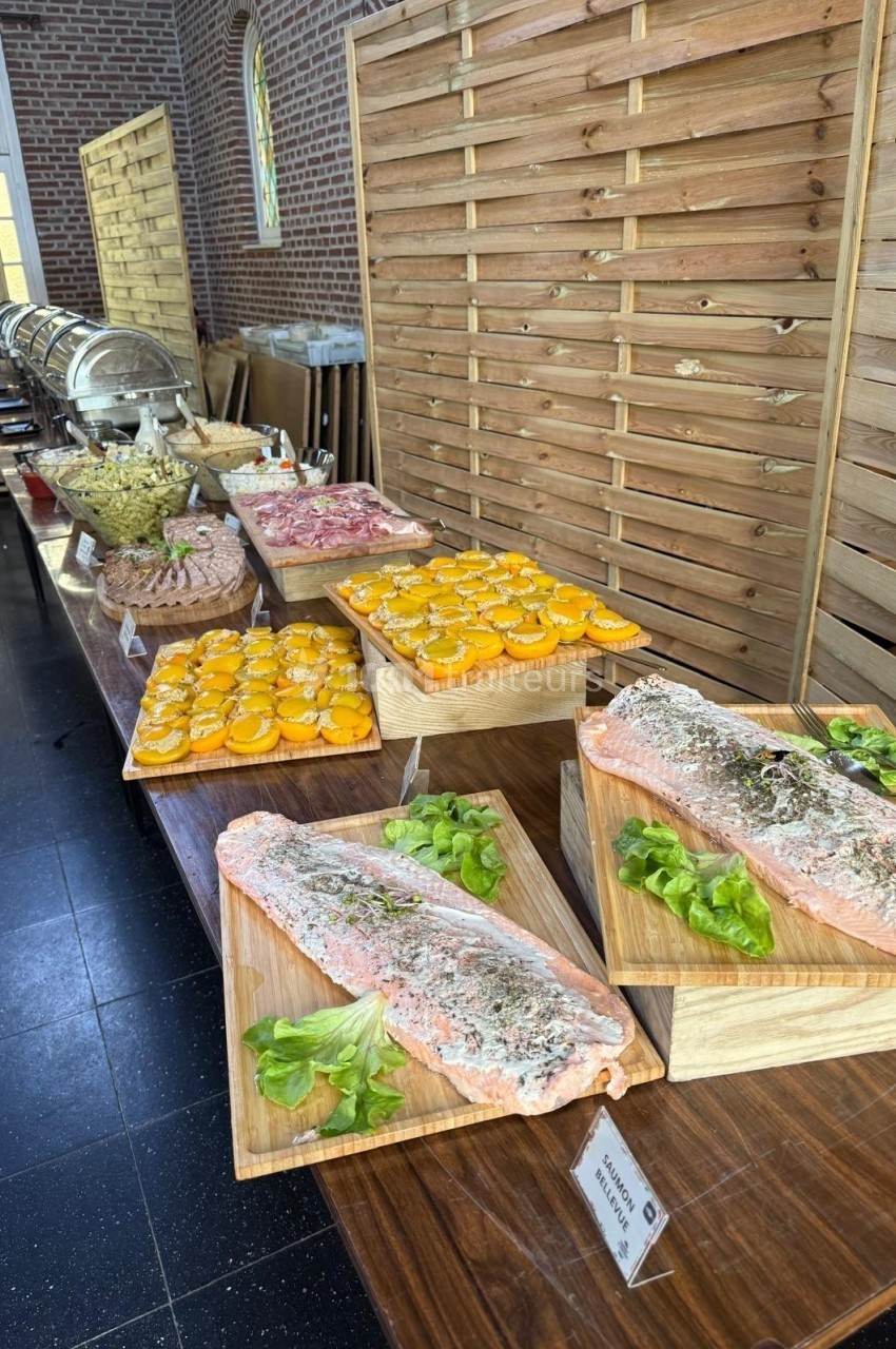 Buffet avec plats variés, incluant du saumon, des tranches d'agrumes et des salades, disposés sur des tables en bois.