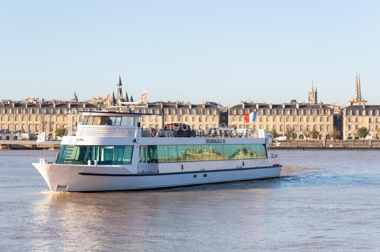 Bateau de croisière naviguant sur un fleuve avec des bâtiments historiques en arrière-plan.