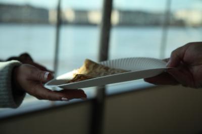 Une personne tend une assiette en carton contenant une crêpe à une autre personne, en arrière-plan flou d'une fenêtre.