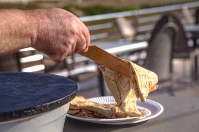 Une personne tend une assiette en carton contenant une crêpe à une autre personne, en arrière-plan flou d'une fenêtre.