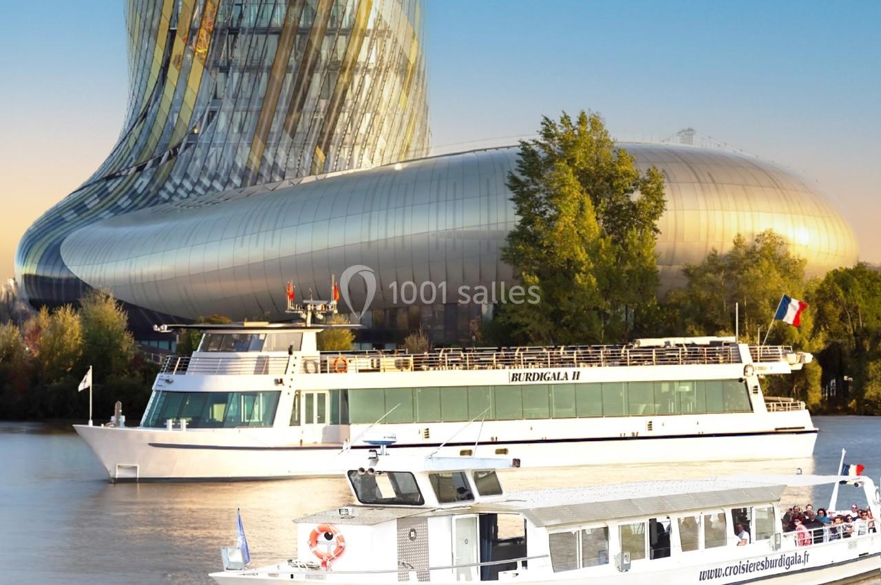 Deux bateaux de croisière naviguent sur une rivière devant un bâtiment moderne aux formes courbées.