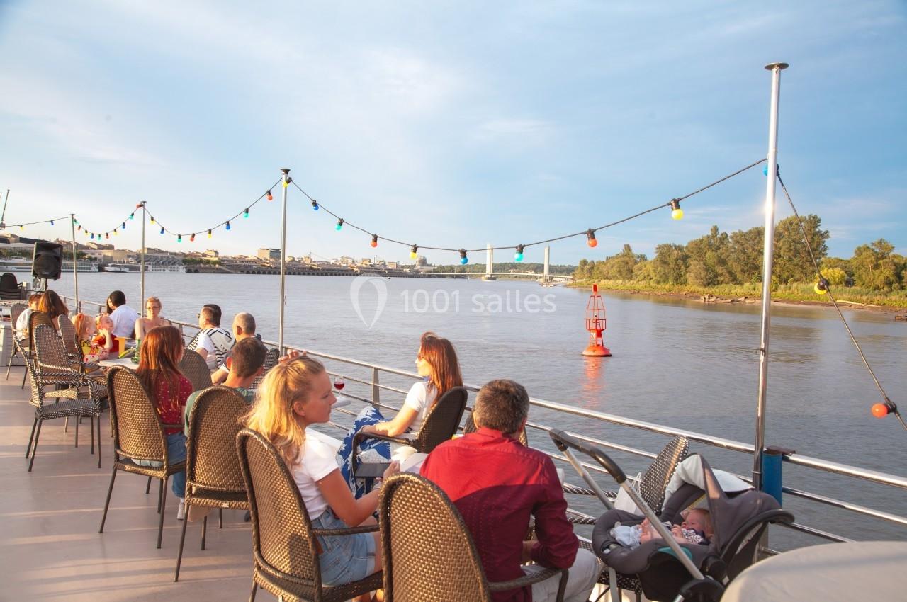 Des personnes assises sur le pont d'un bateau, profitant d'une vue sur une rivière bordée de végétation et de bouées.