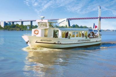 Miniature Aquitania en navigation  Bâtiment moderne en verre et métal près d'un fleuve, avec un bateau blanc amarré au premier plan.