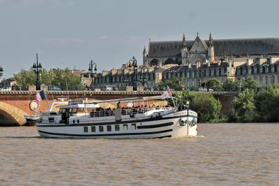 Miniature Burdigala I Pont de Pierre  Bâtiment moderne en verre et métal près d'un fleuve, avec un bateau blanc amarré au premier plan.