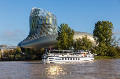 Miniature Burdigala I proche de la Cité du Vin  Bâtiment moderne en verre et métal près d'un fleuve, avec un bateau blanc amarré au premier plan.