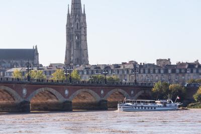 Miniature Burdigala I proche du Pont de Pierre  Bâtiment moderne en verre et métal près d'un fleuve, avec un bateau blanc amarré au premier plan.
