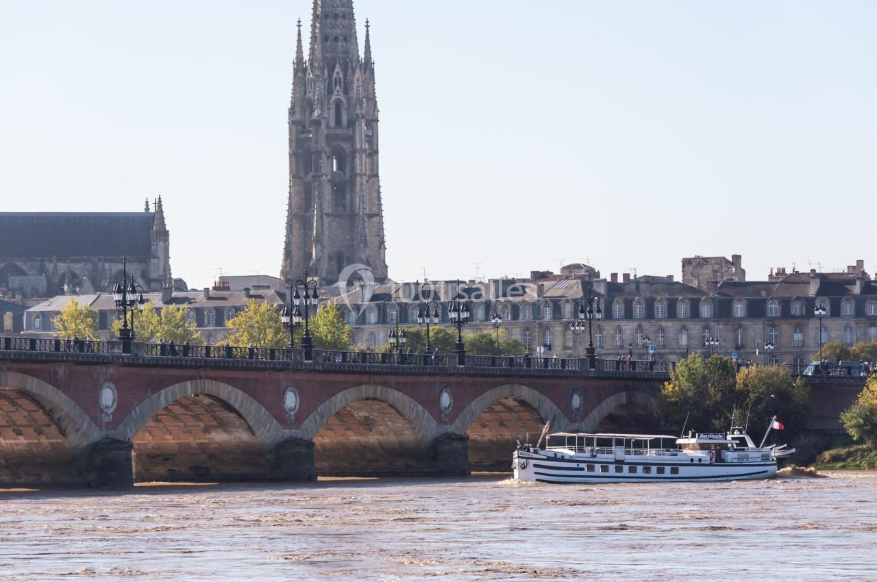 Vue d'un bateau naviguant sur la Garonne devant le pont de pierre et la flèche Saint-Michel à Bordeaux.