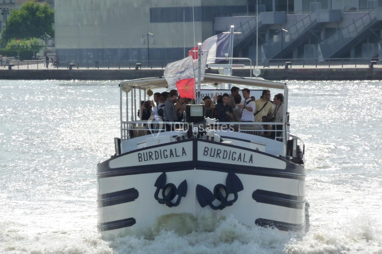 Bateau touristique nommé ’Burdigala’ naviguant sur une rivière par temps ensoleillé, avec des passagers à bord.