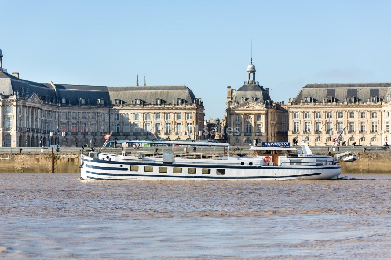 Bateau de croisière naviguant sur un fleuve devant des bâtiments historiques sous un ciel dégagé.