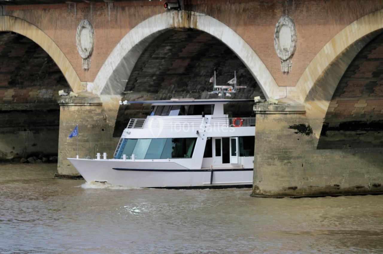 Bateau blanc naviguant sous un pont en briques avec des arches au-dessus d'une rivière.