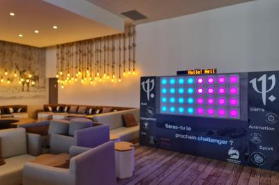 Un homme debout consulte son téléphone dans un espace intérieur décoré avec des lumières et des arbres artificiels.