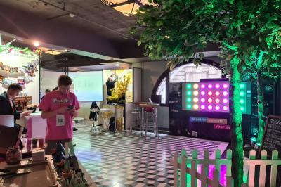 Un homme debout consulte son téléphone dans un espace intérieur décoré avec des lumières et des arbres artificiels.