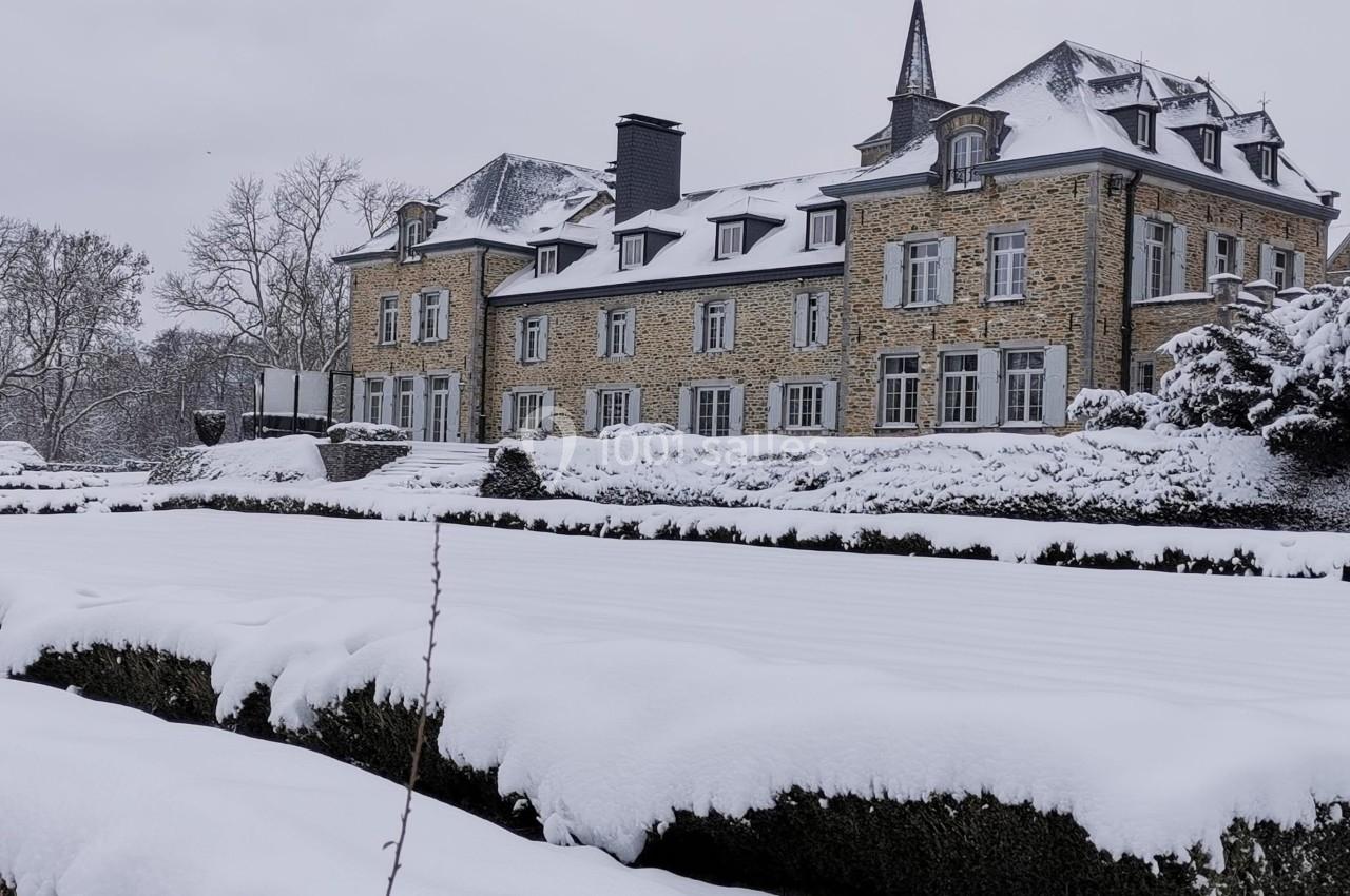 Bâtiment en pierre entouré d'un jardin enneigé sous un ciel gris.