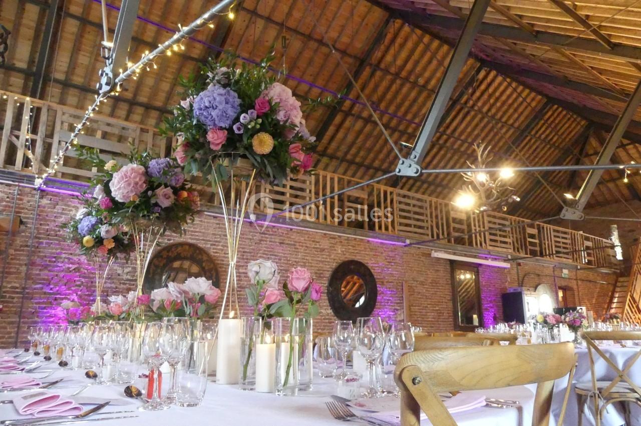 Salle de réception décorée pour un mariage, avec tables dressées, bouquets de fleurs et éclairage tamisé.