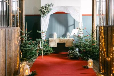 Miniature Location salle Libramont-Chevigny (Luxembourg) - Domaine du Château de Freux #25 Un couple en tenue de mariage se tient devant un officiant dans un décor festif avec sapins et guirlandes lumineuses.