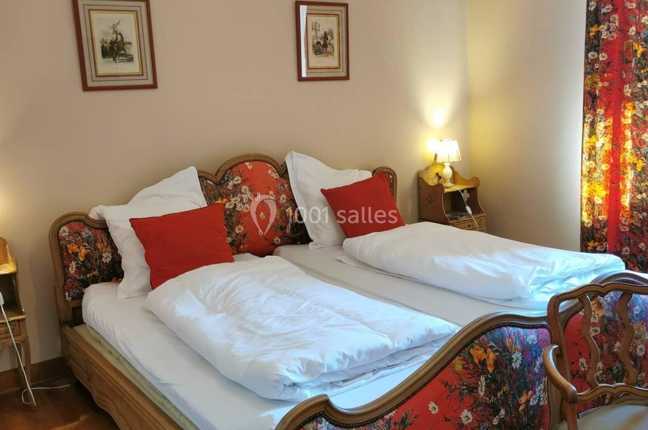 Chambre avec deux lits simples, tête de lit et textiles à motifs floraux, éclairée par des lampes de chevet.