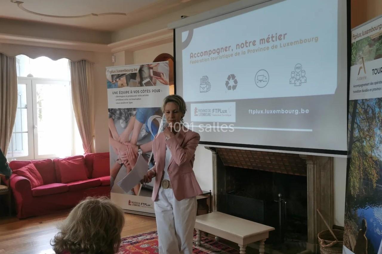 Une femme présente devant un écran affichant des informations sur le tourisme en Province de Luxembourg, dans une salle…