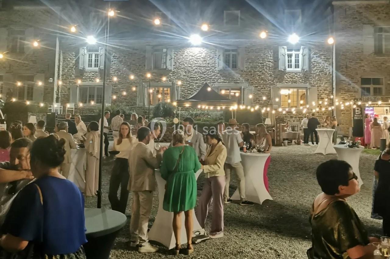 Groupe de personnes discutant debout lors d'une réception en soirée, éclairée par des guirlandes lumineuses.