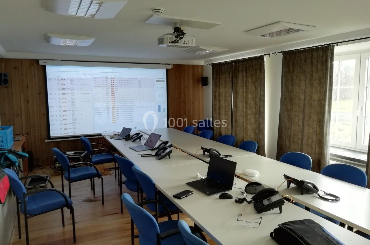 Salle de réunion avec une grande table, des chaises, des ordinateurs, un projecteur et un écran affichant un tableau.
