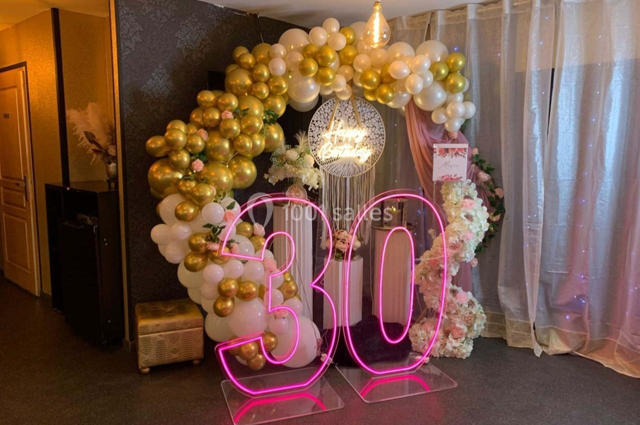 Décoration festive avec arche de ballons blancs et dorés, panneau lumineux et chiffre 30 en néon rose.