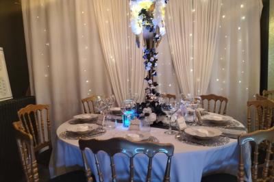 Miniature Silvie Wedding & Events #17 Figurines de mariés sur un gâteau décoré de fleurs bleues, d'une feuille argentée et d'un cœur en arrière-plan.