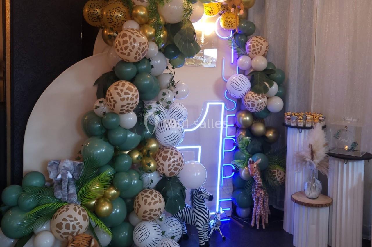 Décoration festive avec ballons verts, blancs et dorés, motifs animaliers, et chiffres lumineux entourés de figurines…