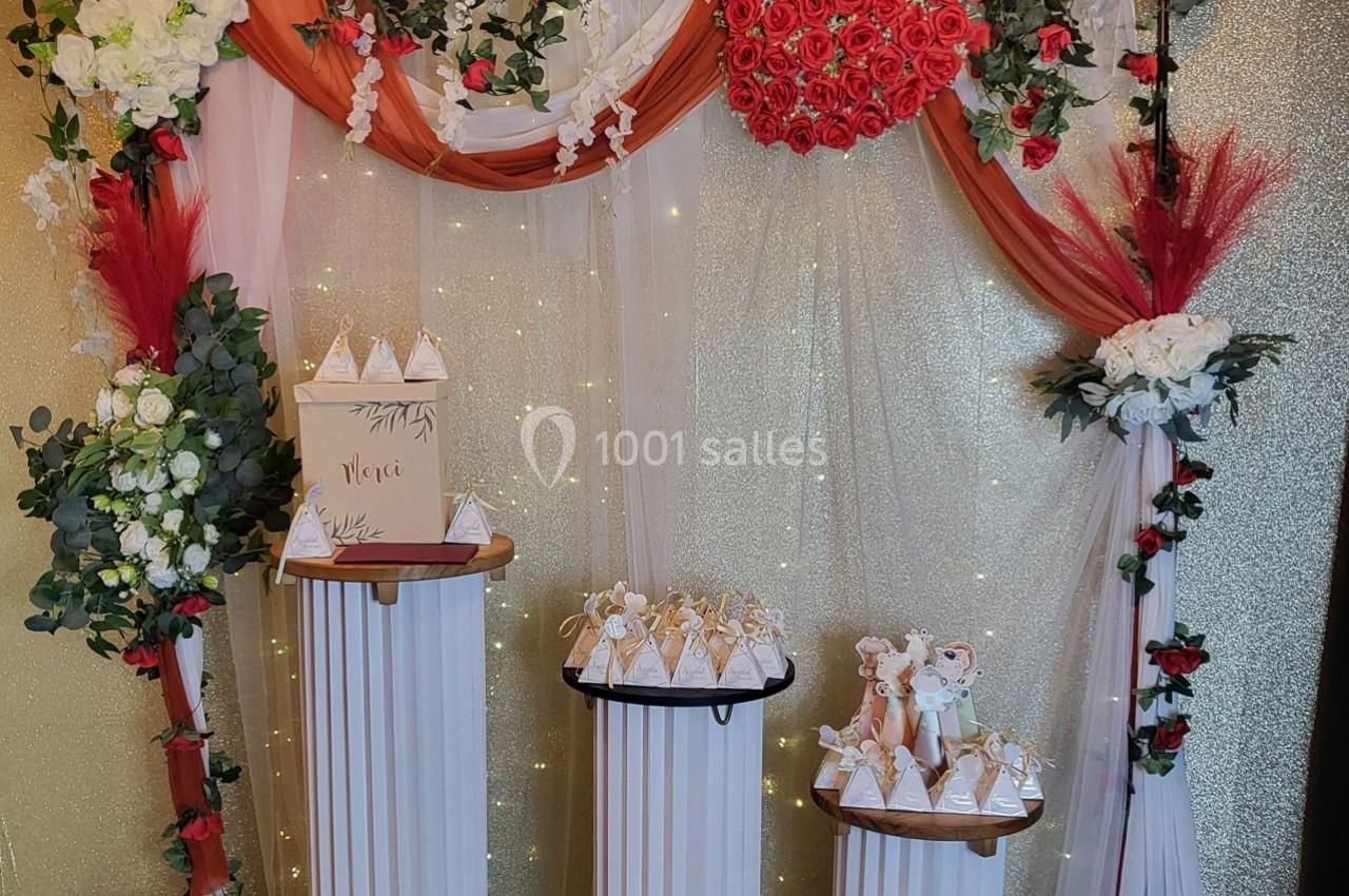 Décoration festive avec colonnes blanches, fleurs rouges et blanches, rideau scintillant et boîtes cadeaux triangulaires.