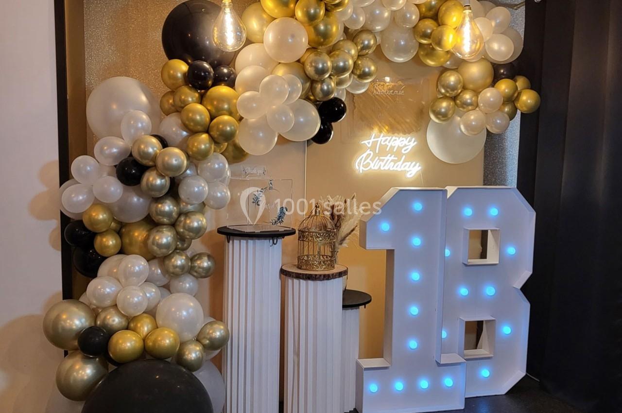 Décoration d'anniversaire avec ballons dorés, blancs et noirs, chiffre lumineux ’18’ et panneau ’Happy Birthday’.