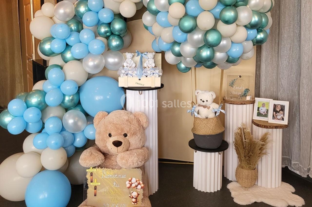 Décoration festive avec ballons bleus et blancs, peluches, cadeaux et éléments décoratifs sur des colonnes blanches.