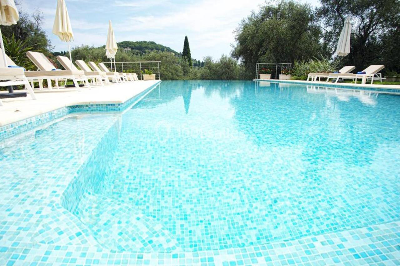 Piscine extérieure avec eau turquoise, entourée de chaises longues et parasols, bordée de végétation.