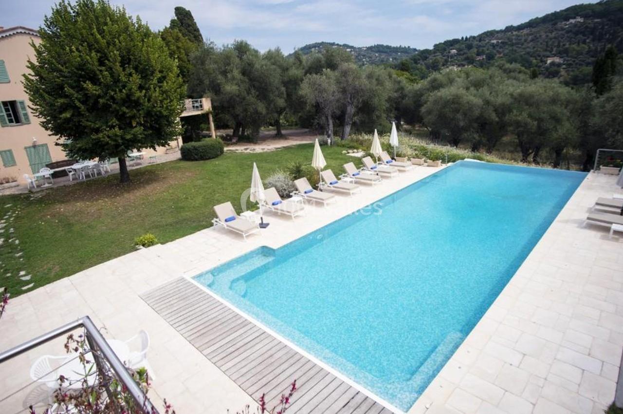 Piscine extérieure entourée de chaises longues et parasols, située dans un jardin arboré avec collines en arrière-plan.
