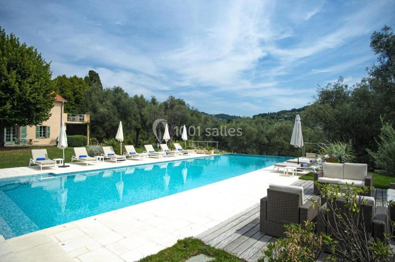 Piscine extérieure entourée de chaises longues, parasols, mobilier de jardin et végétation sous un ciel dégagé.