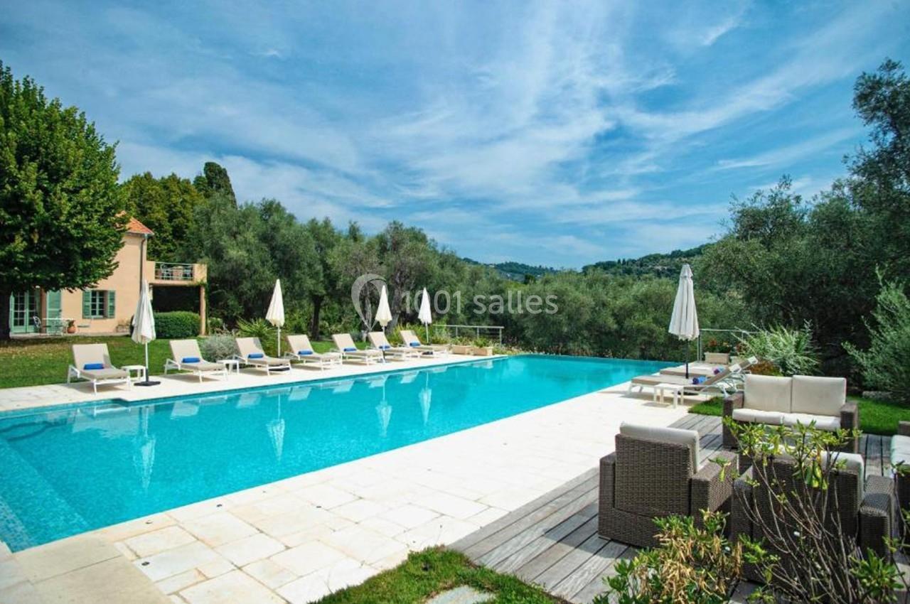 Piscine extérieure entourée de chaises longues, parasols, mobilier de jardin et végétation sous un ciel dégagé.