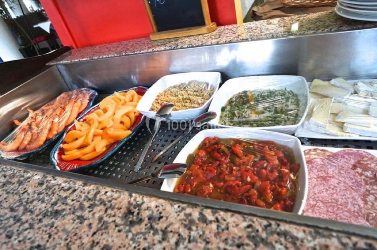 Buffet avec divers plats froids : crevettes, melon, légumes, charcuterie et fromages, présentés sur un comptoir en marbre.