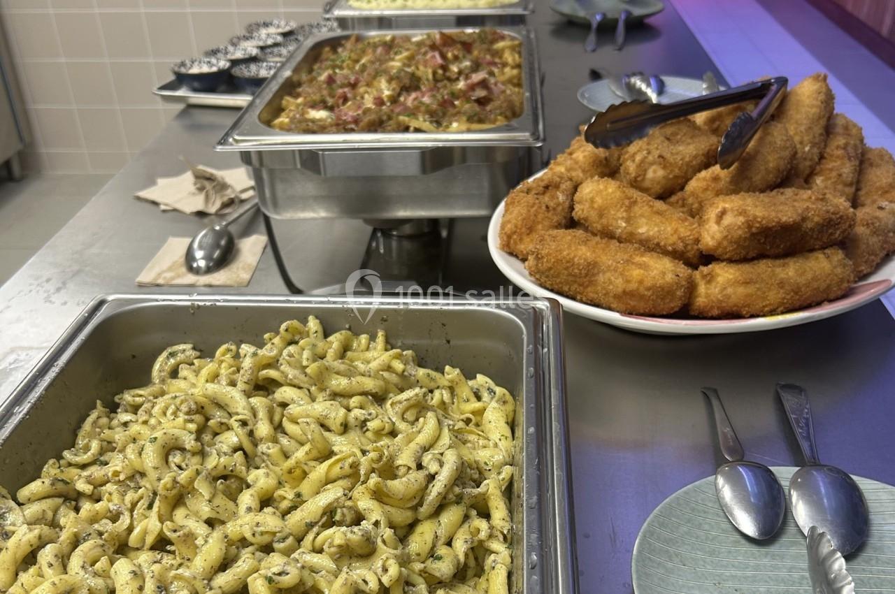 Buffet avec des pâtes assaisonnées, gratin de légumes et croquettes dorées, présenté sur un comptoir en inox.