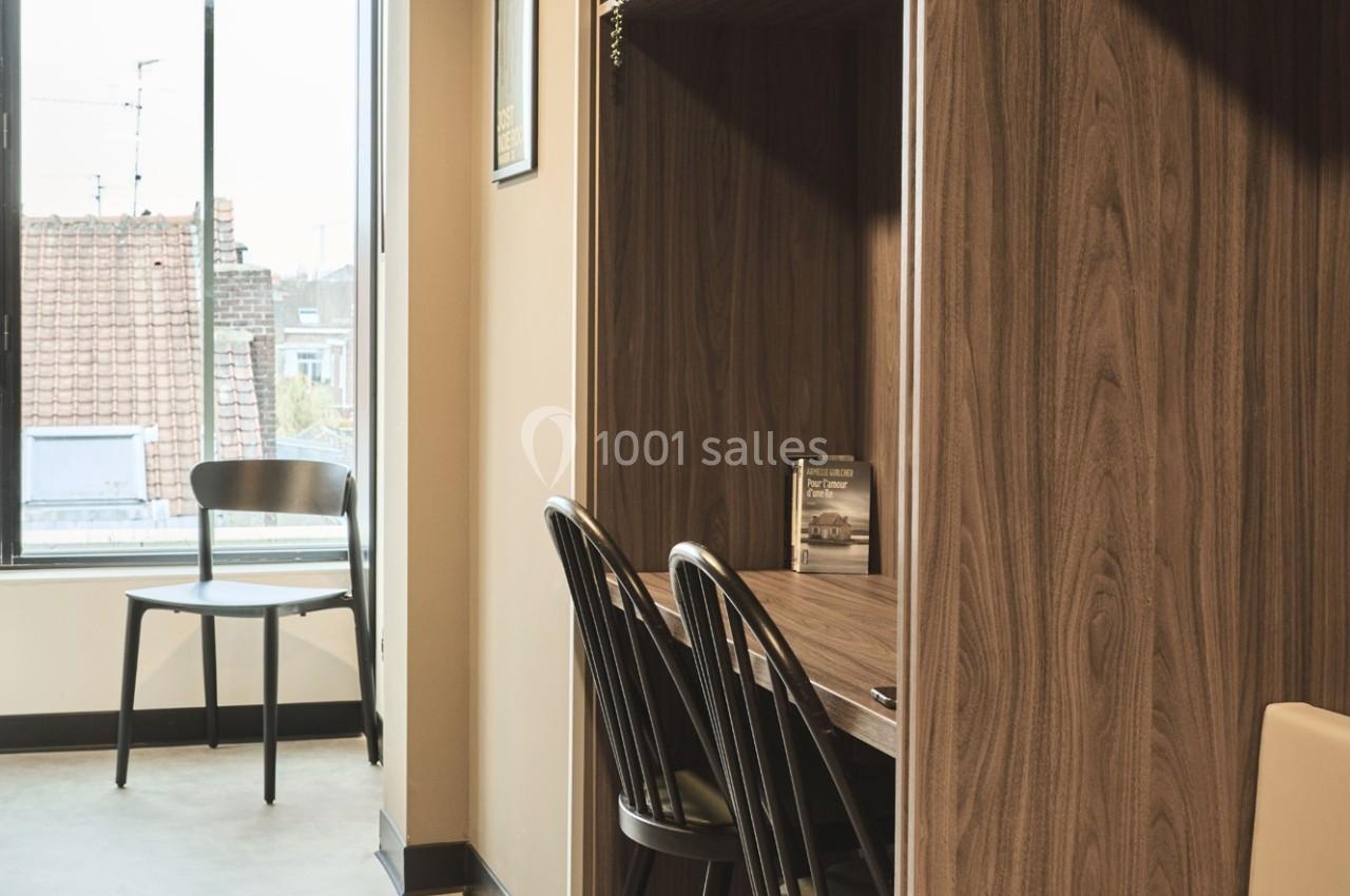 Espace de travail en bois avec deux chaises, une fenêtre donnant sur des toits et une chaise supplémentaire à côté.