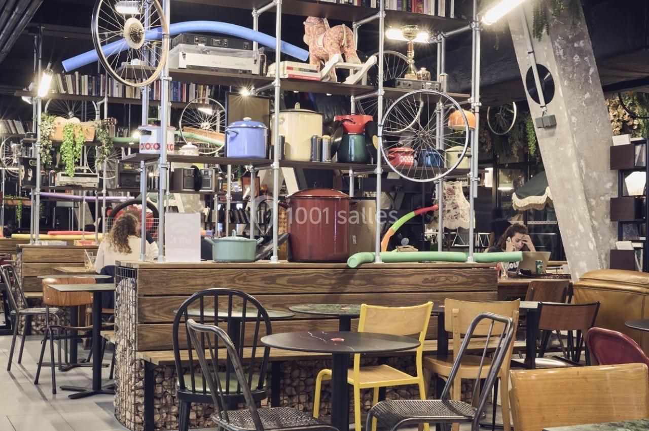 Salle de restaurant éclectique avec mobilier varié et étagères décorées d'objets divers, dont des roues et des ustensiles.