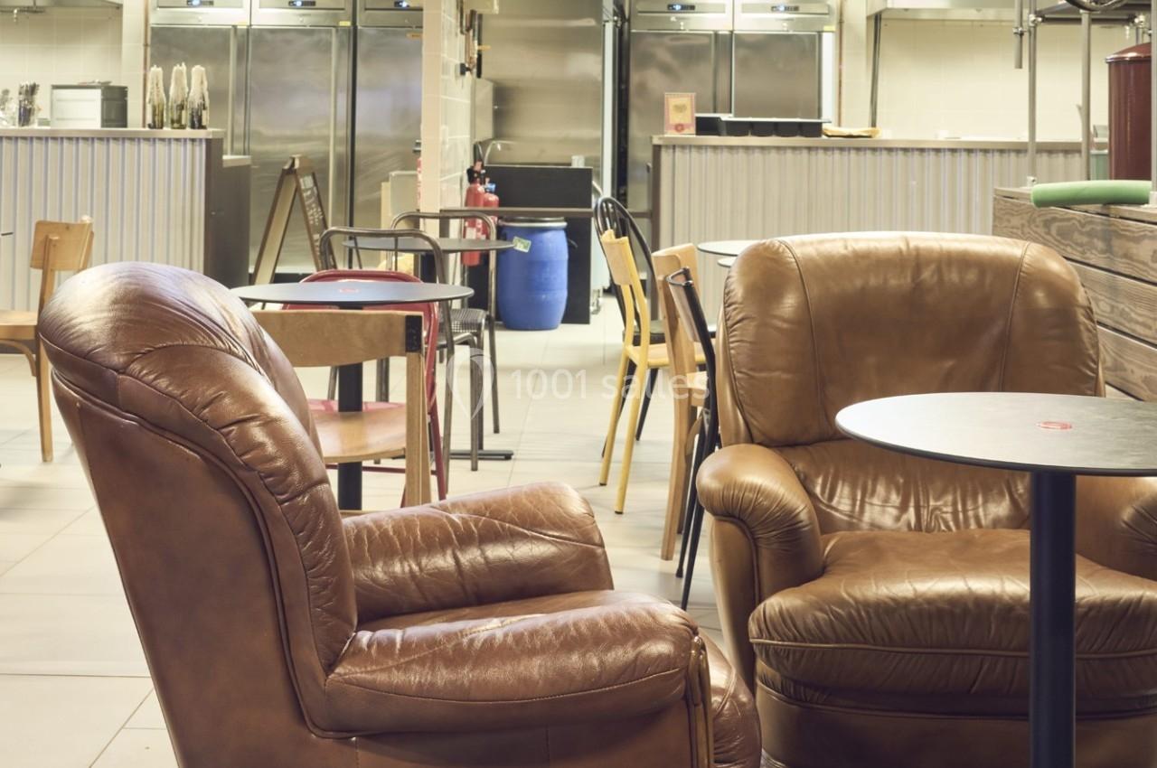 Deux fauteuils en cuir marron et des tables dans un espace intérieur lumineux avec un comptoir en arrière-plan.