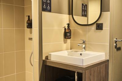 Lavabo moderne avec miroir, distributeur de savon mural et carrelage beige dans une salle de bain.