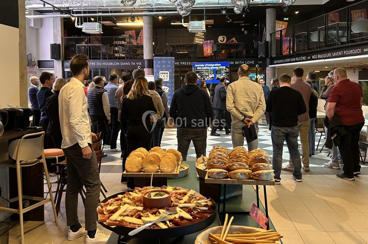 Groupe de personnes debout dans un espace intérieur, avec des tables garnies de snacks et de pains au premier plan.