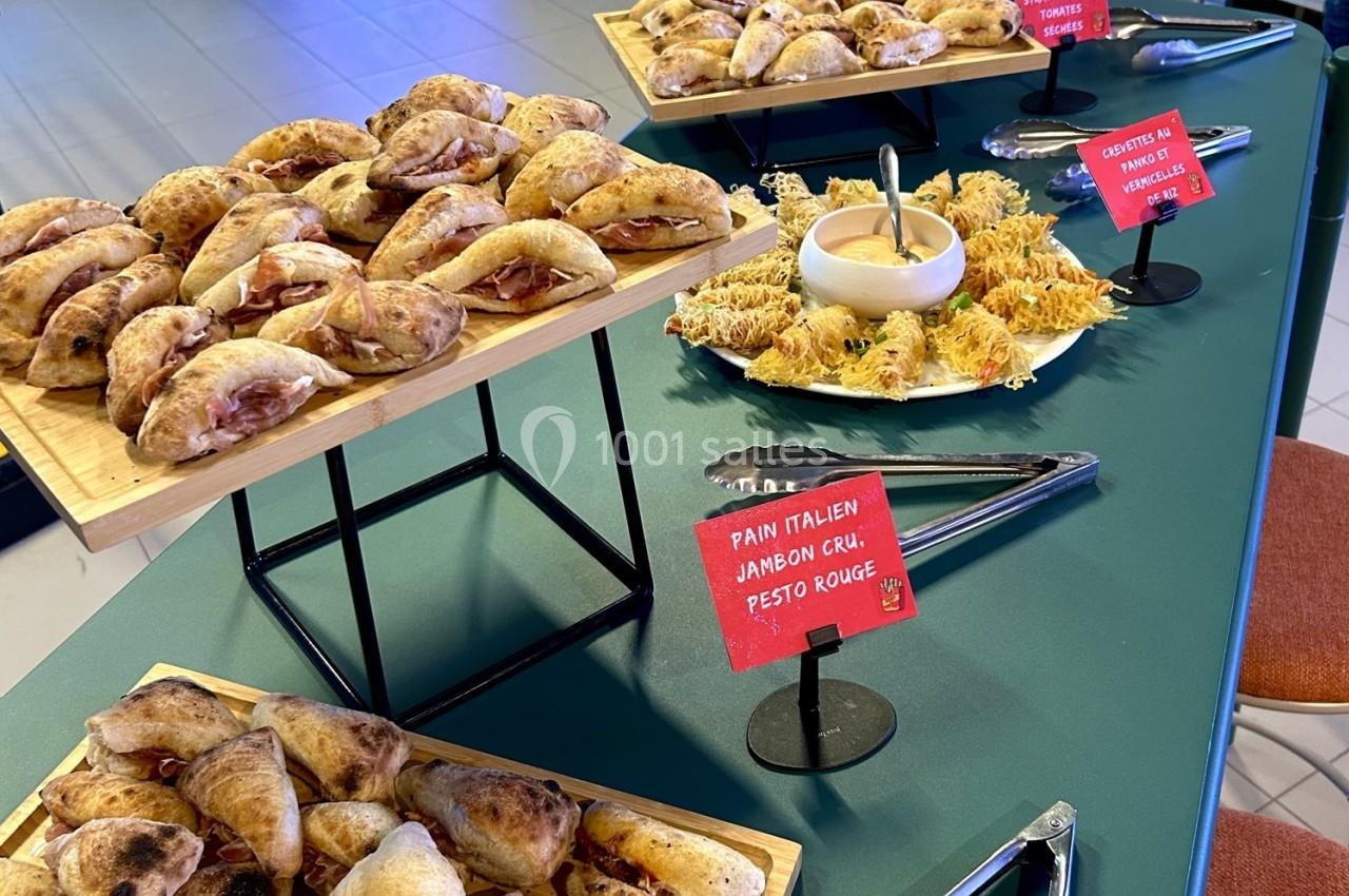 Buffet avec mini-sandwichs au jambon cru et pesto rouge, crudités et fromage râpé, disposés sur des plateaux.
