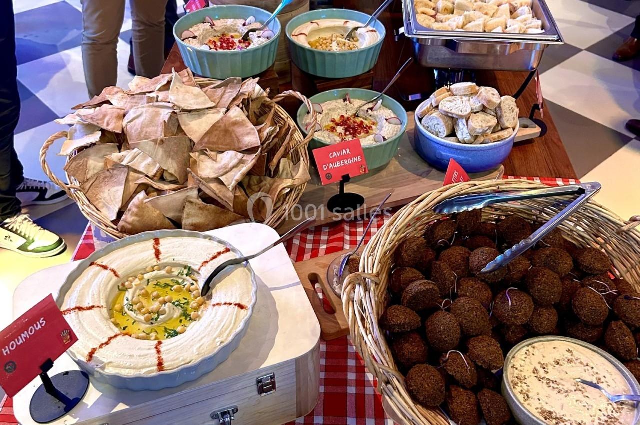 Buffet varié avec houmous, falafels, pains pita, mezzés, œufs farcis et plats chauds sur une nappe à carreaux rouges.