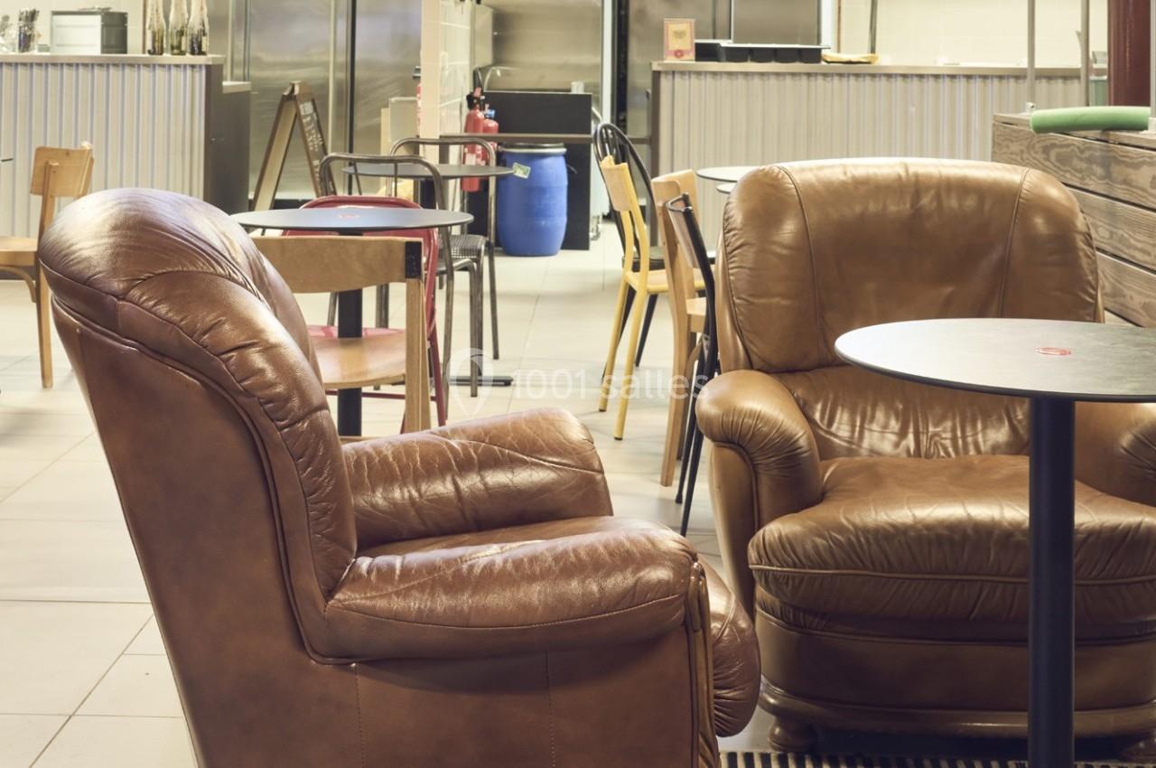 Deux fauteuils en cuir marron disposés autour d'une table dans un espace intérieur avec des chaises et un comptoir en…