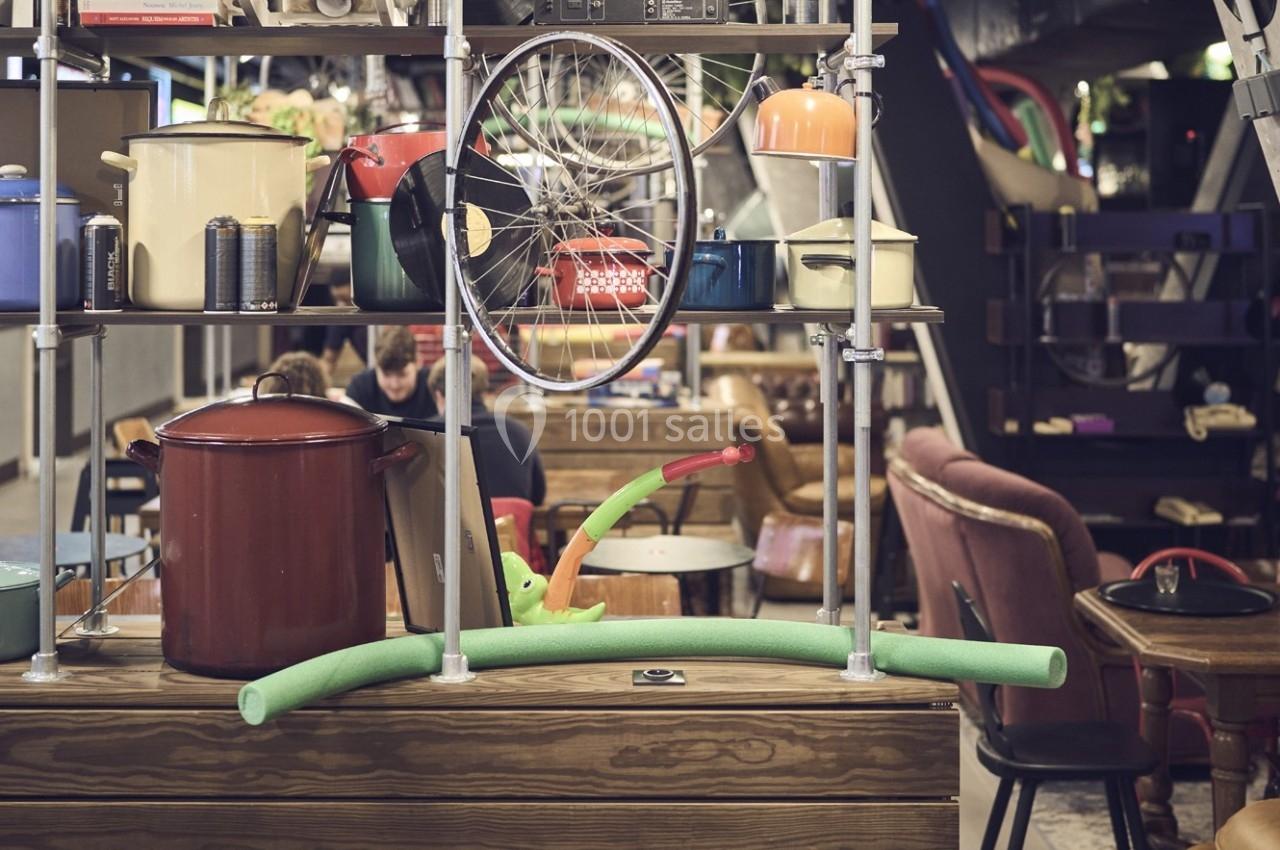 Étagère avec objets variés, dont une roue de vélo, des casseroles et un jouet, dans un espace de café animé.