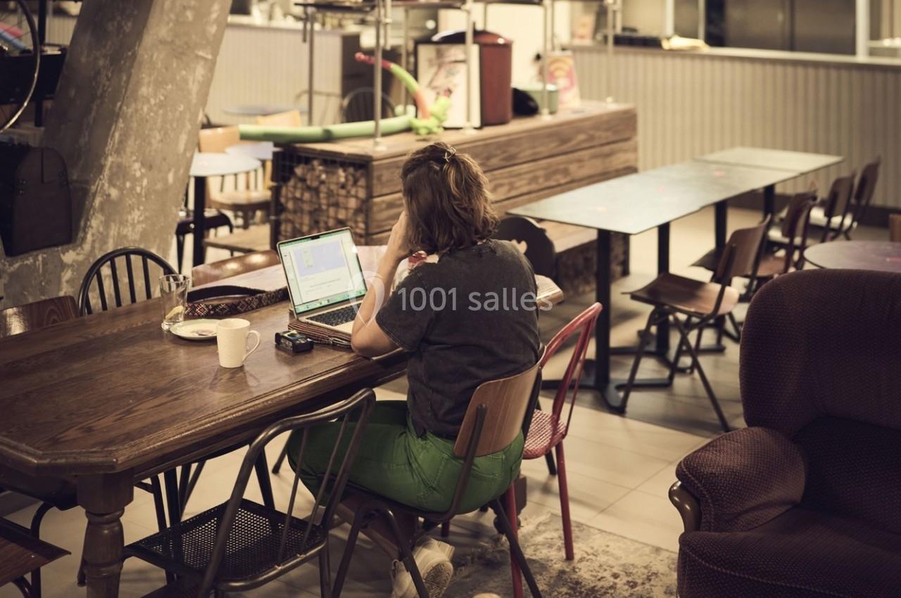 Une personne travaille sur un ordinateur portable dans un espace intérieur avec des tables et des chaises en bois.