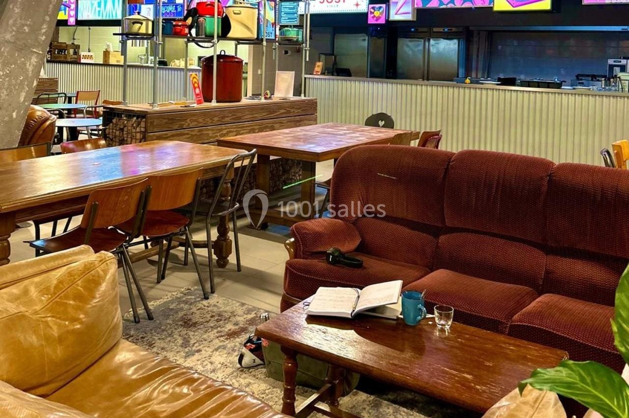 Espace intérieur avec canapés, tables en bois, livre ouvert et tasse sur une table basse, ambiance décontractée.