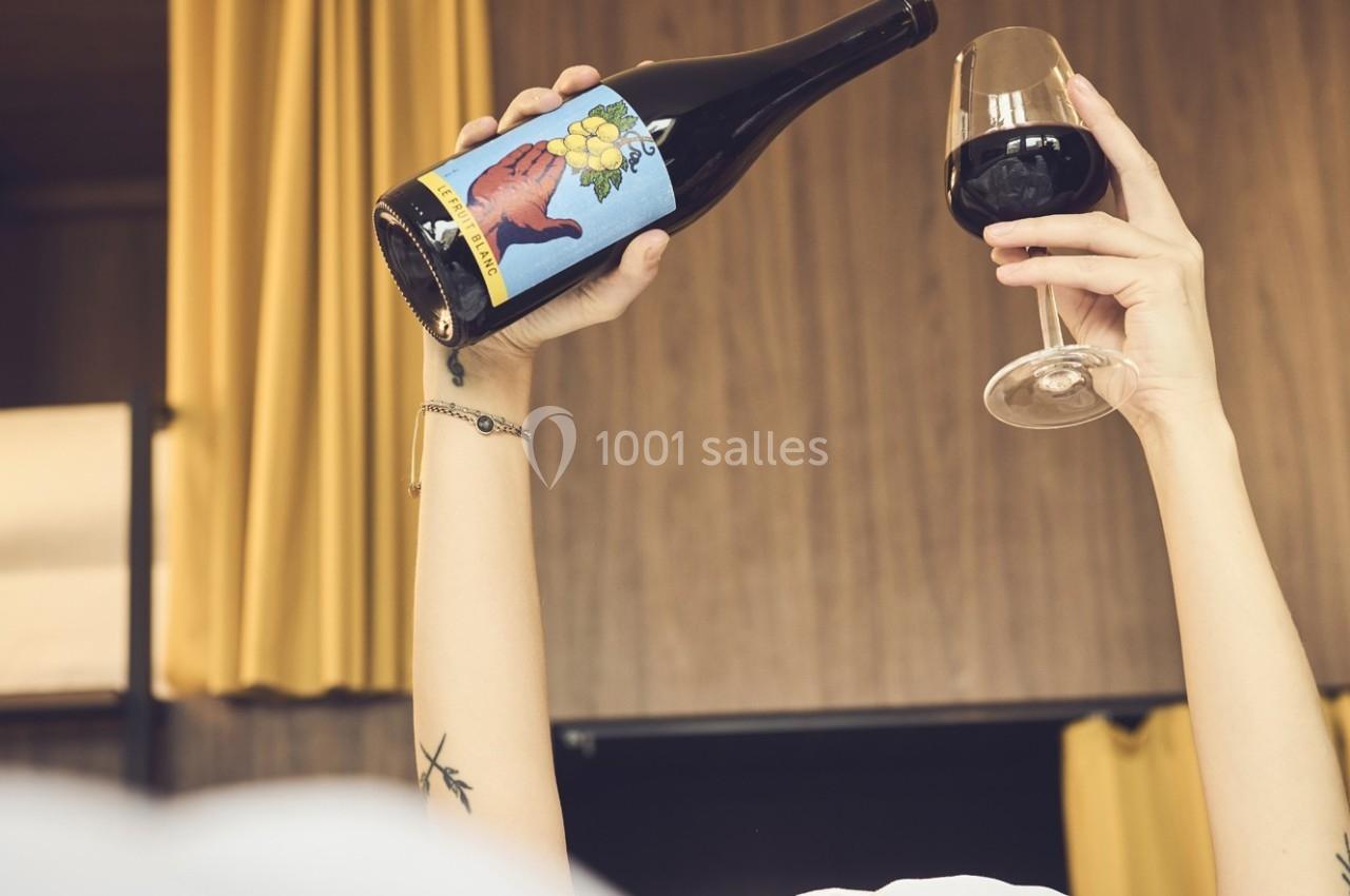 Une main tient une bouteille de vin avec une étiquette colorée, tandis qu'une autre main lève un verre de vin rouge.