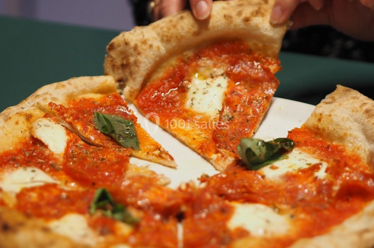 Part de pizza margherita avec sauce tomate, mozzarella fondue et feuilles de basilic, servie sur une assiette blanche.